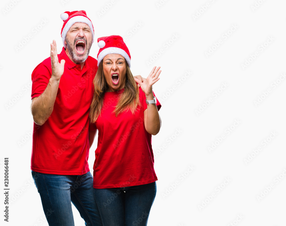 Middle age hispanic couple wearing christmas hat over isolated background crazy and mad shouting and yelling with aggressive expression and arms raised. Frustration concept. Middle age hispanic couple wearing christmas hat over isolated background crazy and mad shouting and yelling with aggressive expression and arms raised. Frustration concept.
