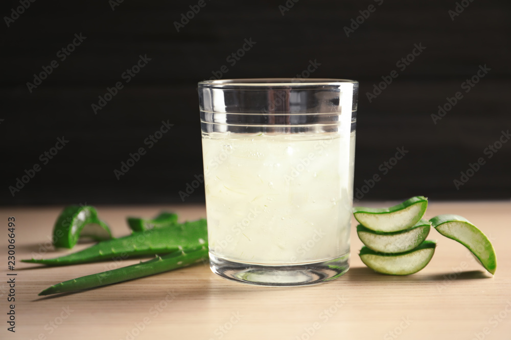 Glass with aloe vera juice and green leaves on wooden table against dark background Glass with aloe vera juice and green leaves on wooden table against dark background