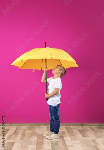 Little boy with yellow umbrella near color wall