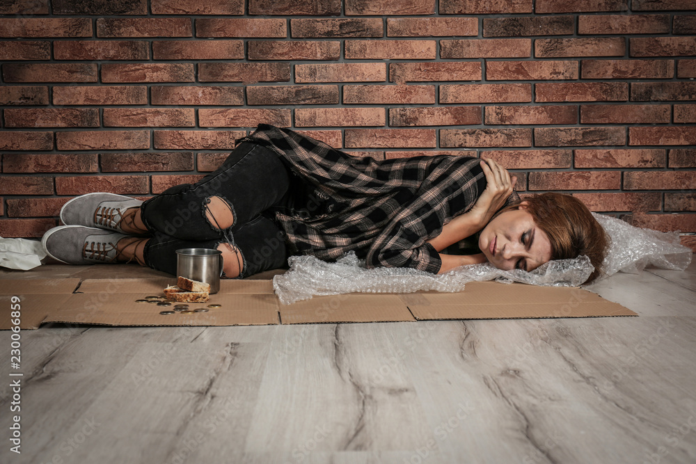 Poor homeless woman sleeping on floor near brick wall Stock Photo