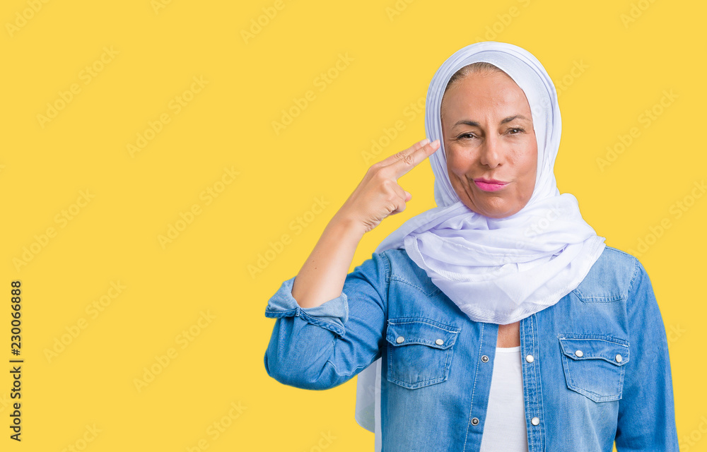 Portrait of mature woman showing hand gun gesture against yellow background Portrait of mature woman showing hand gun gesture against yellow background