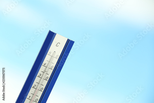 Weather thermometer and blue cloudy sky on background. Space for text