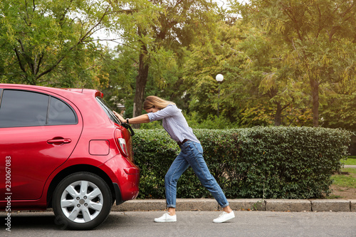 Woman pushing broken car on road along city street