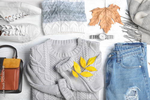 Stylish outfit and autumn leaves on white wooden background, flat lay. Trendy warm clothes