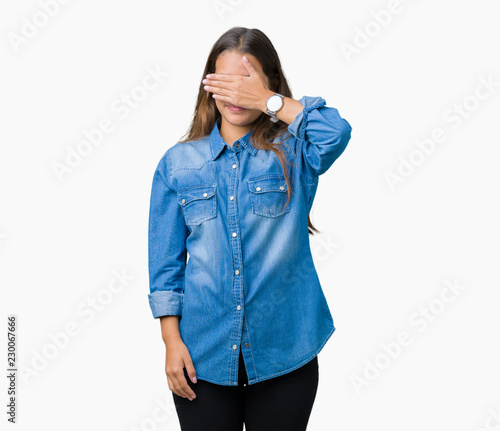 Young beautiful brunette woman wearing blue denim shirt over isolated background smiling and laughing with hand on face covering eyes for surprise. Blind concept.