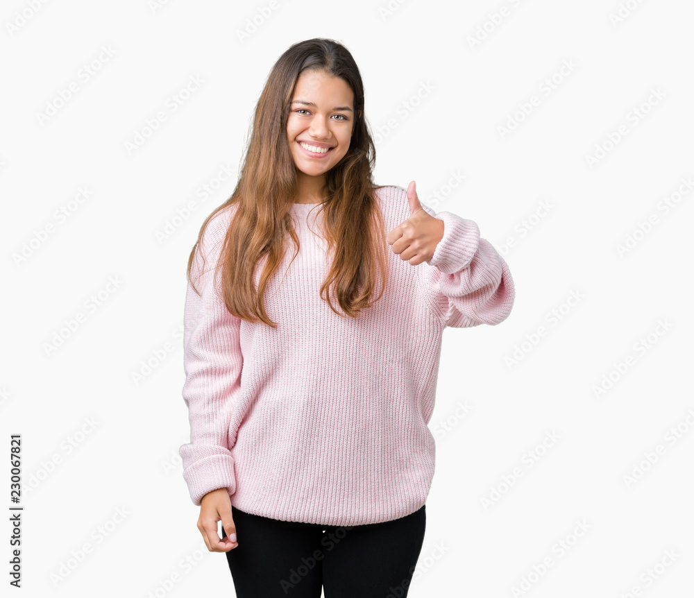 Young beautiful brunette woman wearing pink winter sweater over isolated background doing happy thumbs up gesture with hand. Approving expression looking at the camera showing success.