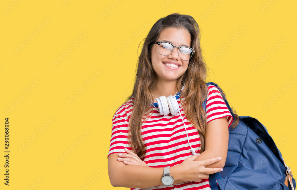 Young beautiful brunette student woman wearing headphones and backpack over isolated background happy face smiling with crossed arms looking at the camera. Positive person.