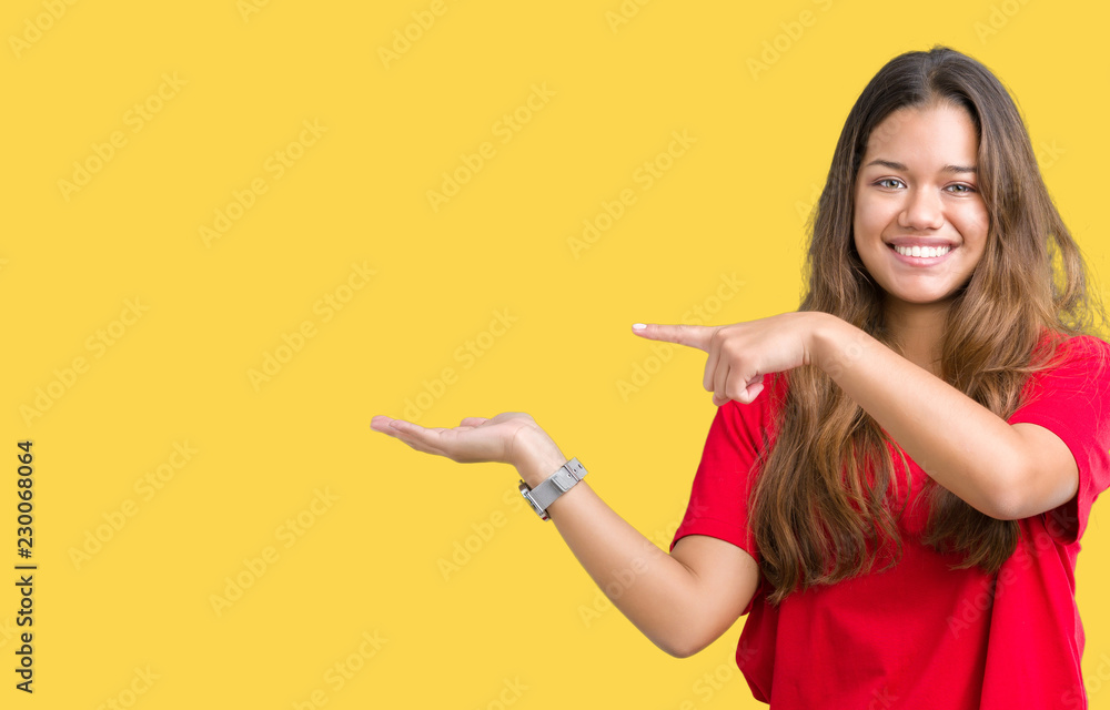 Young beautiful brunette woman wearing red t-shirt over isolated background amazed and smiling to the camera while presenting with hand and pointing with finger. Young beautiful brunette woman wearing red t-shirt over isolated background amazed and smiling to the camera while presenting with hand and pointing with finger.