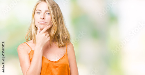 Beautiful young woman wearing orange shirt over isolated background looking confident at the camera with smile with crossed arms and hand raised on chin. Thinking positive.