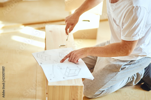 Concentrated young man reading instructions to assemble furniture at home photo