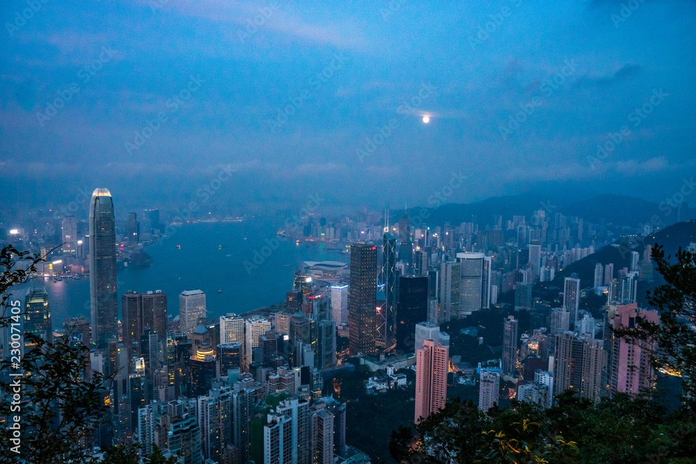 Full moon rise over Hong Kong Skyline at dusk. Modern China city with skyscrapers near the ocean
