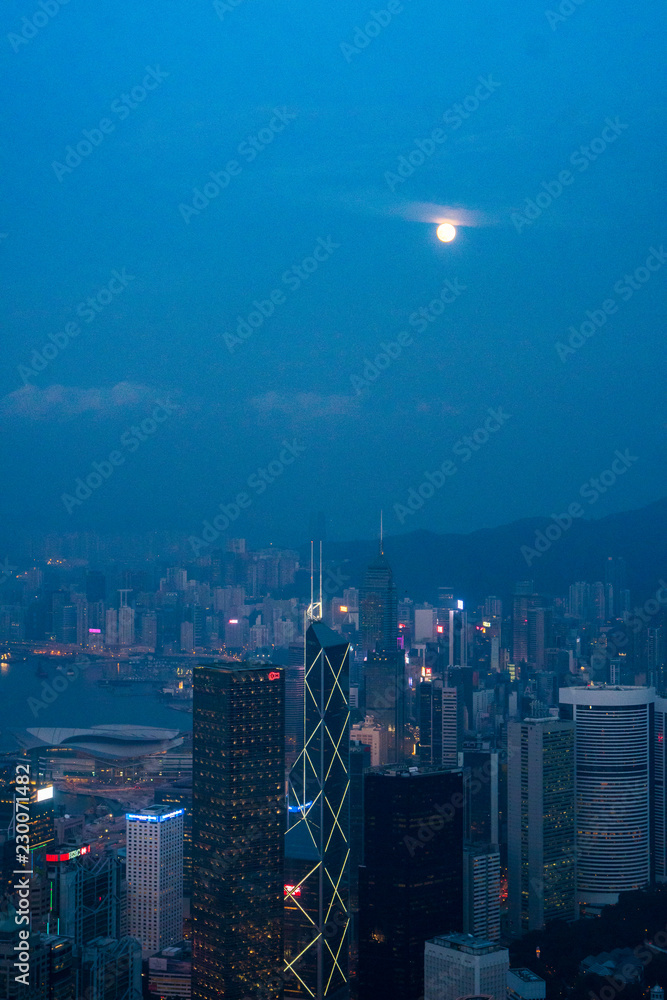 Fototapeta premium Full moon rise over Hong Kong Skyline at dusk. Modern China city with skyscrapers near the ocean