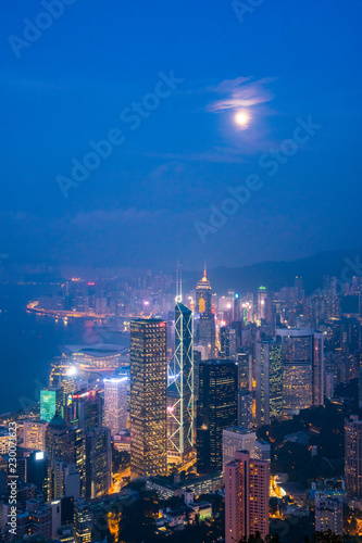 Full moon rise over Hong Kong Skyline at dusk. Modern China city with skyscrapers near the ocean