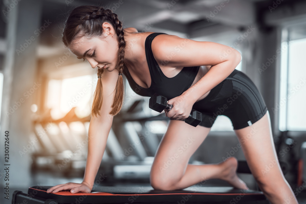 Fototapeta premium Cinematic tone of young attractive fitness woman exercise with dumbbell in gym. Individual sport to fit muscles of body for healthy life concept. 