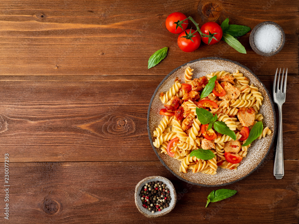 fusilli pasta with tomato sauce, chicken fillet with basil leaves on dark brown wooden background, copy space, top view fusilli pasta with tomato sauce, chicken fillet with basil leaves on dark brown wooden background, copy space, top view