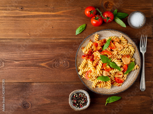 fusilli pasta with tomato sauce, chicken fillet with basil leaves on dark brown wooden background, copy space, top view