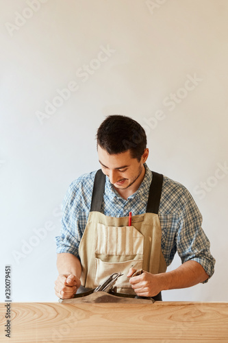 Skilled caucasian man wearing casual checkered shirt and apron working in his woodwork workshop, using a handplaner hobby concept. photo