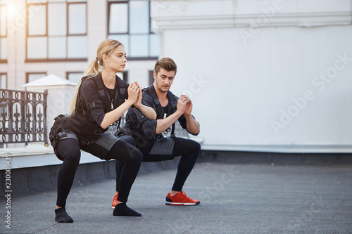 two fit young people bending knees to full squat position. side view full length photo. copy space. photo