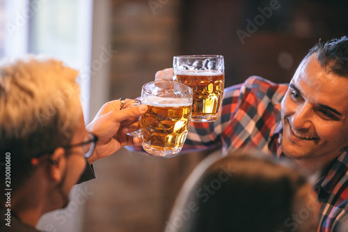 Two friends (men) cheering (clinking) with glasses of beer - friends party and holidays celebration concept