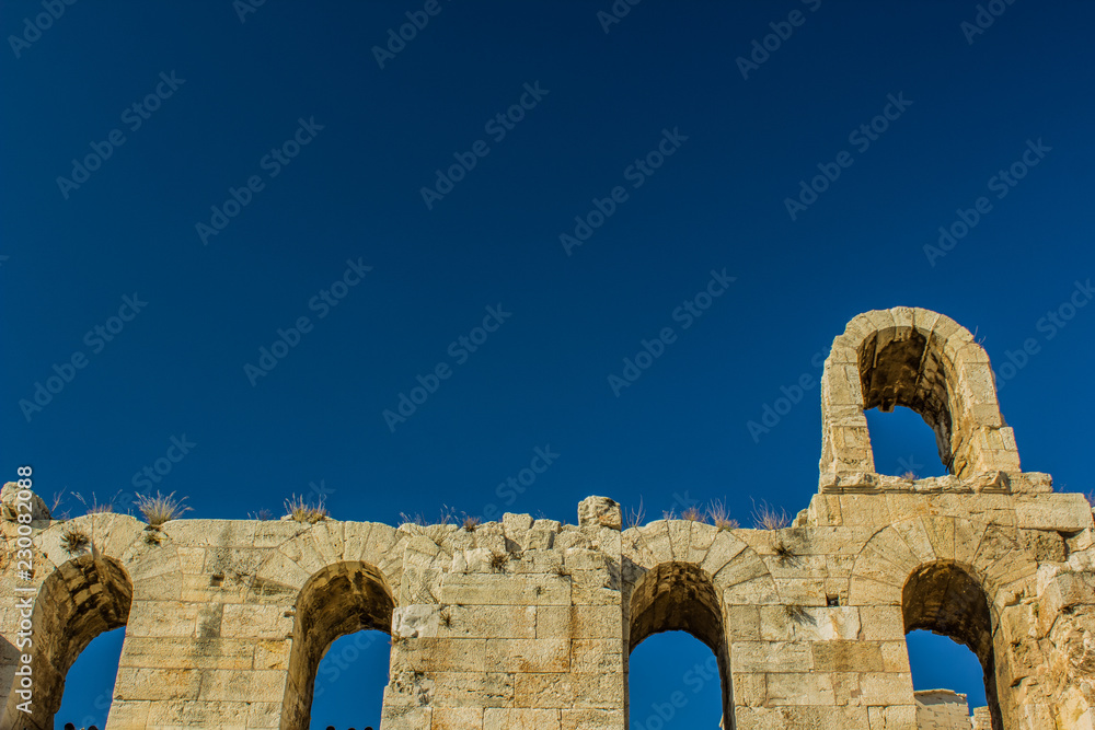 ancient stone ruins of wall with arch shapes windows on empty blue sky background, copy space