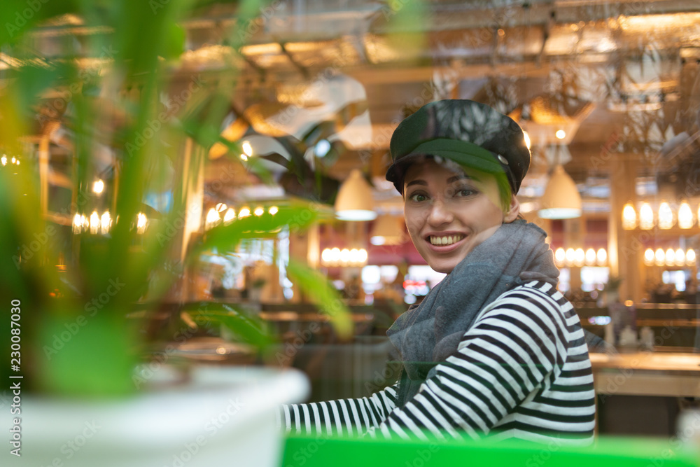 beautiful woman in hat and scarf drinking coffee while sitting in cafe
