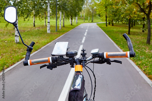View from the side of the cyclist. Handlebar of a brutal bicycle against the background of a bicycle path going into perspective among green trees