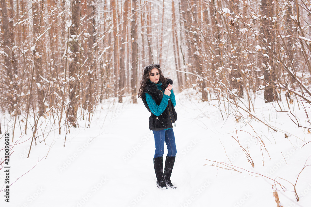 Naklejka premium Young pretty woman walking in the winter snowy park at sunny day
