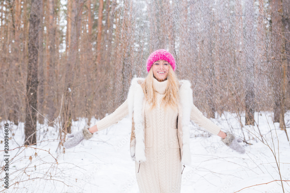 Fototapeta premium Winter, walks and people concept - young blond woman walking in the winter forest and throwing the snow up