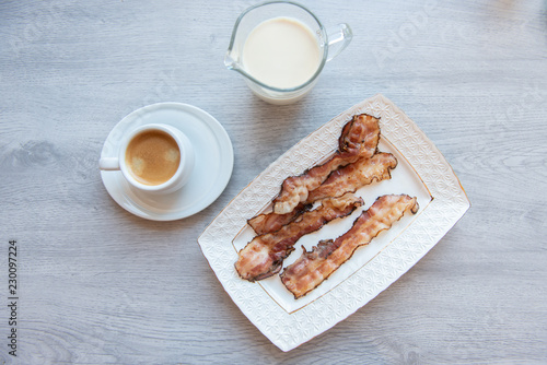 Fried bacon on white plate with cup of coffee and milk jug