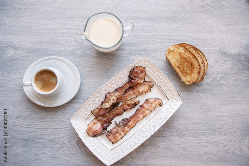 Fried bacon on white plate with cup of coffee and milk jug