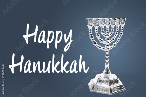 Happy Hanukkah and winter holidays concept with a silver menorah isolated on blue background with the text Happy Hanukkah in white next to it