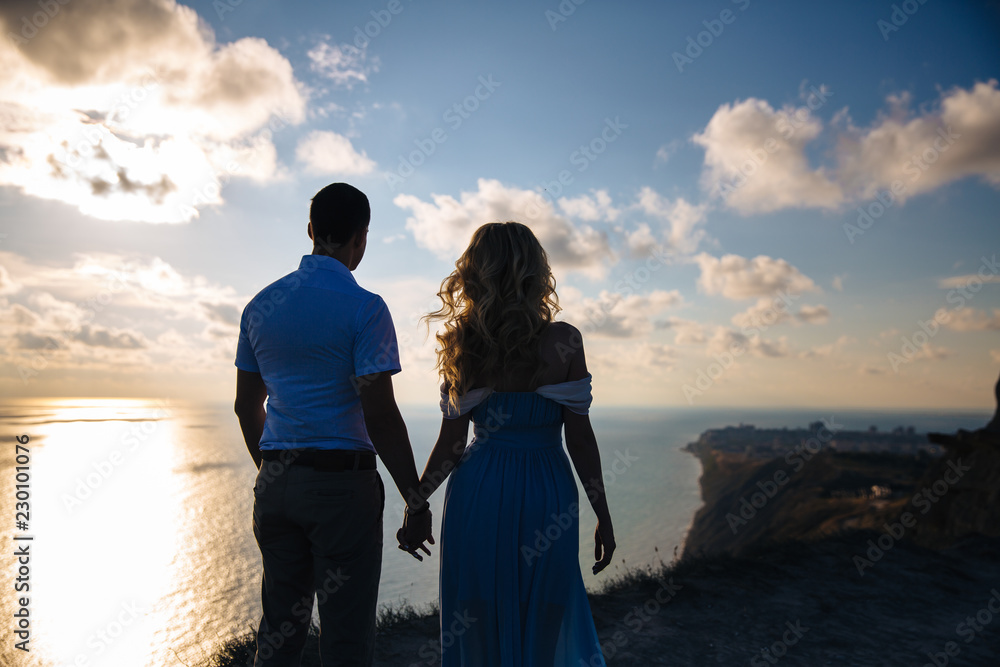 Silhouette of a loving couple at sunset. Man embracing with a woman on a high mountain overlooking the sea. Concept family, love, wedding, honeymoon trip.