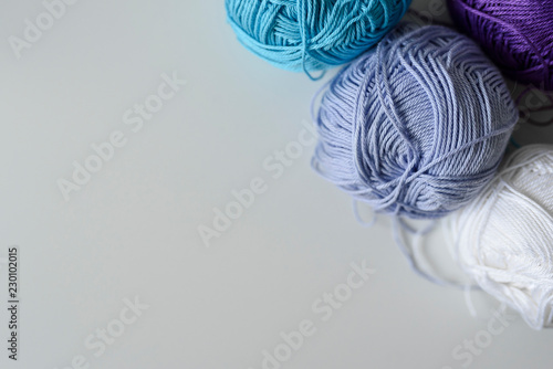 Purple, blue and white knitting yarn balls for handicraft in the corner of image as a decoration above copy space on white table background.