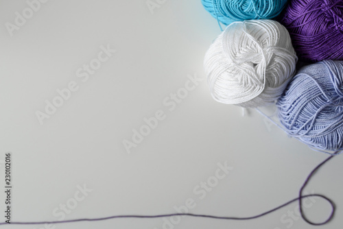 Creative handicraft background from colorful yarn balls in the corner of image, and a purple thread as a bottom frame with copy space on white background.