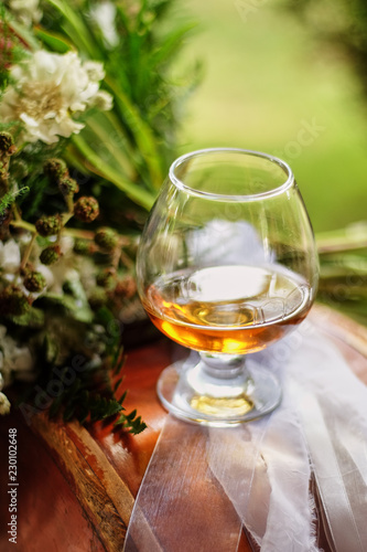Glasses filled with brandy, one glass on the table next to the flower arrangement