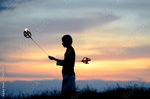 Poi artist swinging flaming tethered weights at sunset