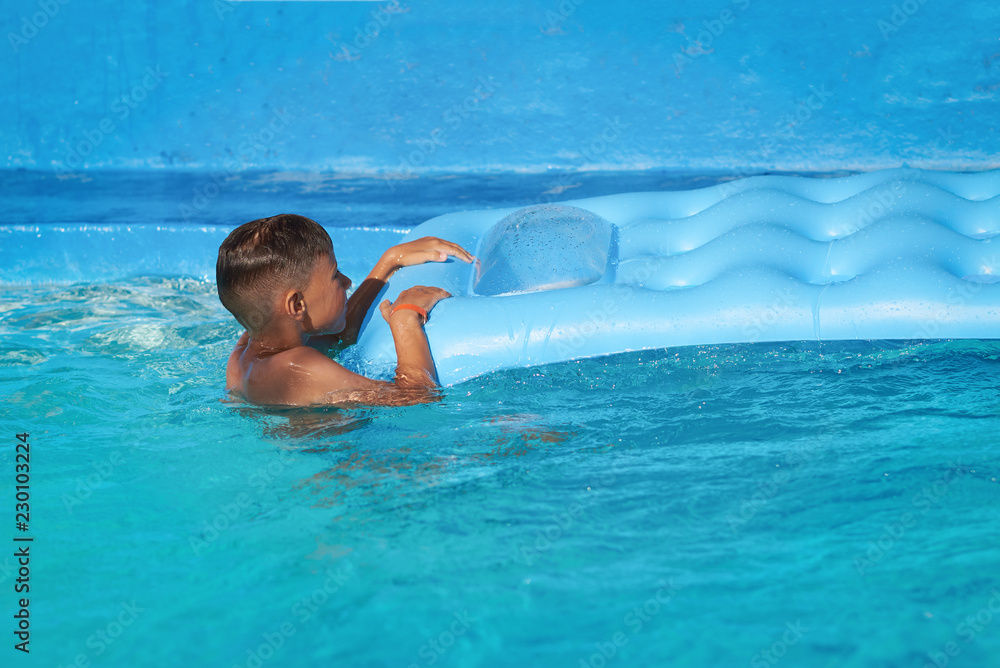 Caucasian boy trying to get out from water on inflatable mattress in swimming pool at resort on summer vacation.