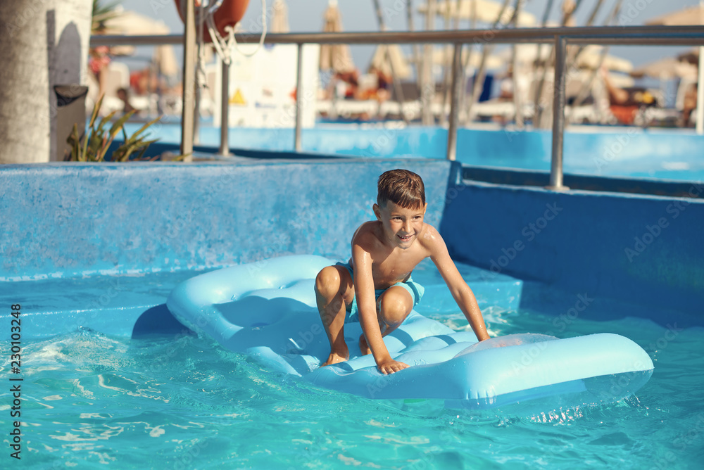 Smiling Boy ready to jump from inflatable mattress into swimming pool at resort.