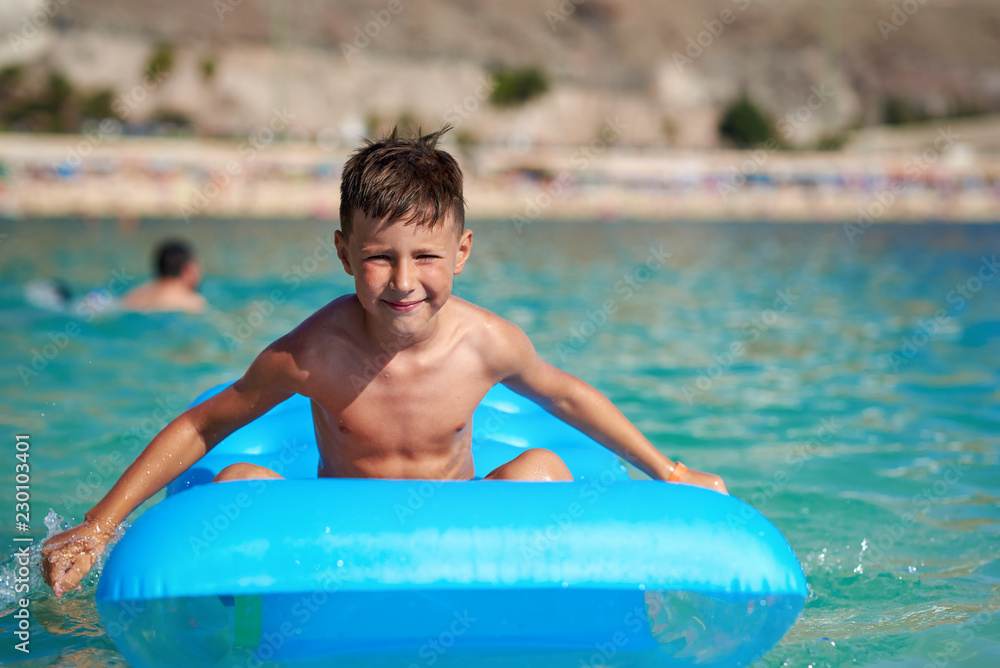 The portrait of cute European boy. He is sitting on the blue inflatable floater, enjoying his holidays and smiling to the camera.