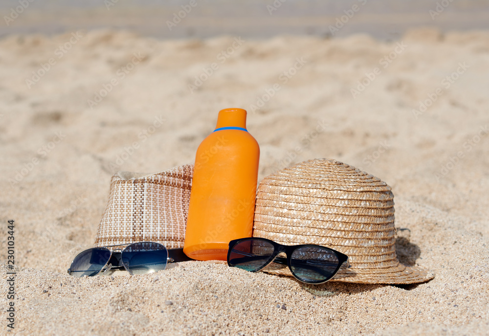 Two sunhats, sunglasses and sunscreen crean are laying on the sand near the sea, illustrating healthy way of life. Two sunhats, sunglasses and sunscreen crean are laying on the sand near the sea, illustrating healthy way of life.