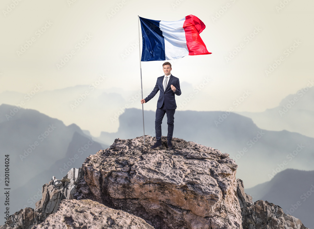 Obraz premium Successful businessman on the top of a mountain holding France victory flag 