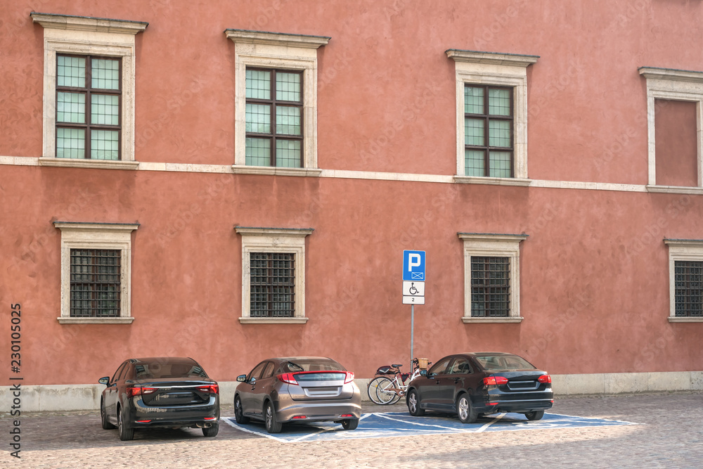 Three cars are parked on a square in the historic part of the city near the sign disabled parking.