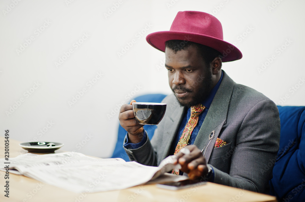 Stylish African American man model in gray jacket tie and red hat drink coffee at cafe and read newspapers. Stylish African American man model in gray jacket tie and red hat drink coffee at cafe and read newspapers.