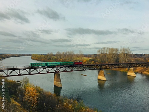 Old train crosses the river on the bridge in autumn