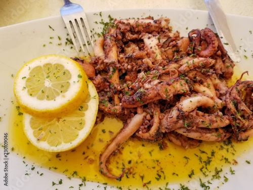 Fried octopus with lemon and spices on white plate with fork and knife in summer street cafe in Marsaxlokk, Malta