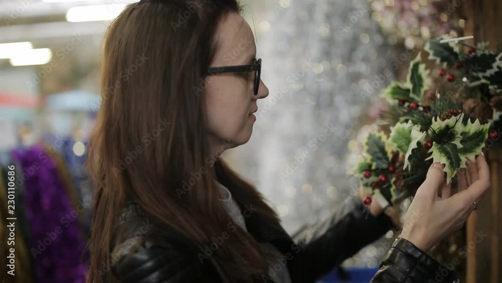 Girl with glasses at the supermarket chooses a Christmas wreath. Girl with glasses at the supermarket chooses a Christmas wreath.