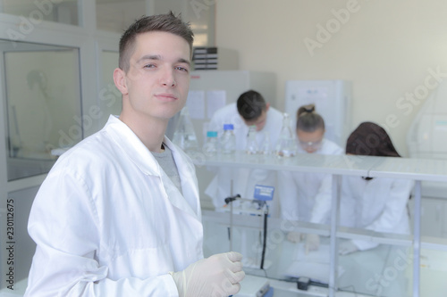 Fototapeta Naklejka Na Ścianę i Meble -  Group of young  scientists doing experiments in laboratory with young scientist male in front posing
