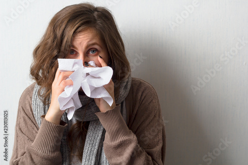 young caucasian woman with curly hair in sweater and scarf blows her nose in a paper handkerchief
