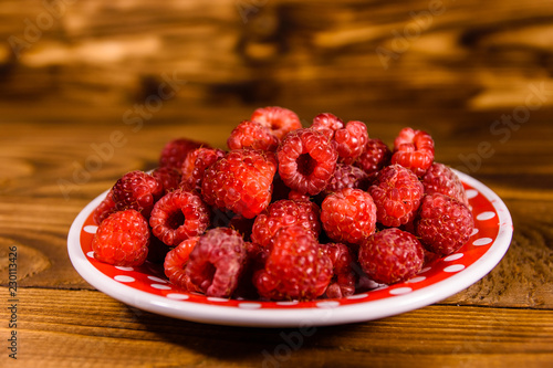 Ceramic plate with ripe raspberries on wooden table