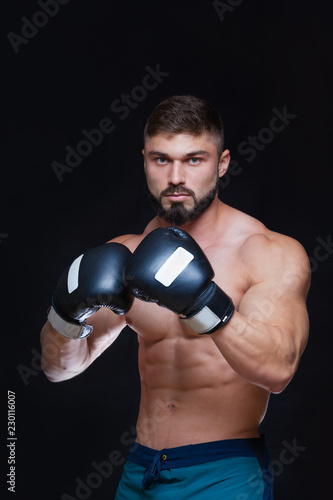 Strong muscular boxer in black boxing gloves. Isolated on black background. © satyrenko